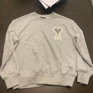 Ami sweatshirt - Snygg grå sweatshirt från Ami Alexandre Mattiussi med stor broderad hjärtdetalj och bokstaven A på bröstet. Tröjan har rund hals, ribbade muddar och är långärmad. Perfekt för dig som gillar stilrena och coola detaljer.