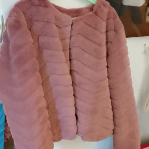 Rosa pälsjacka med vågigt mönster - Säljer en fluffig rosa pälsjacka med vågigt mönster. Jackan har rund halsringning och långa ärmar, och är tillverkad i mjukt syntetmaterial som ger en lyxig känsla. Perfekt för dig som vill sticka ut med en cool och trendig look.