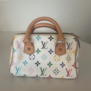 vit handväska med färgglatt mönster - Säljer en vi handväska multicolor monogram i blått, grönt, rött, gult, lila och svart. Väskan har klassiska bruna handtag i skinn och guldfärgade metalldetaljer. Perfekt storlek för det viktigaste och stängs med dragkedja.