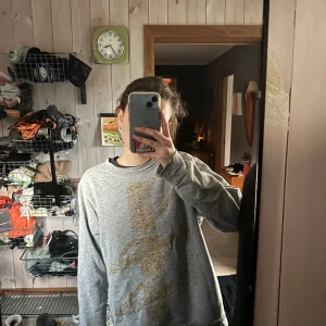 Grå sweatshirt från Carin Western - Säljer en chill grå sweatshirt med ett stort gult/guldigt ”Carin W” tryck på framsidan. Tröjan har rund hals och långa ärmar, perfekt att slänga på sig till jeans. Materialet känns mjukt och skönt, troligen bomull eller polyester. Passformen är normal och avslappnad.
