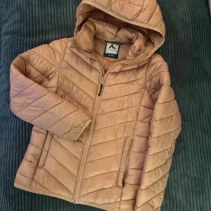 Ljusrosa pufferjacka/dunjacka från McKinley - Säljer en beige pufferjacka från McKinley i storlek 134/140. Jackan har huva, dragkedja framtill och två sidofickor. Den quiltade designen ger en snygg look och jackan är perfekt för kyliga dagar. Passformen är normal och materialet är syntet.