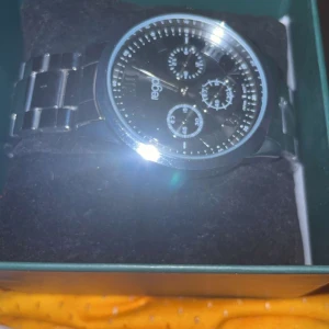 Svart och silver klocka från Regal - Stilren klocka från Regal med svart urtavla och flera små urtavlor. Klockan har ett klassiskt armband i silverfärgad metall och tydliga indexmarkeringar. Perfekt accessoar för dig som gillar en modern och clean look.