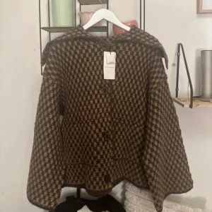 Brun och beige rutig kappa från Zara - Säljer en unik kappa från Zara med brunt och beige rutmönster. Jackan har bred krage, stora knappar framtill och långärmade ärmar. Materialet är ullblandning som ger en mysig och retro känsla. Perfekt för dig som gillar statement-plagg och vintagevibe. Slutsåld på Zara 