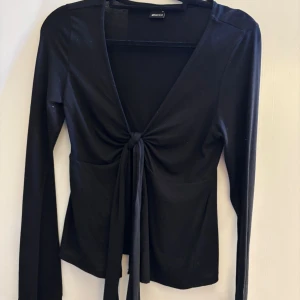 Svart topp från Gina Tricot - Svart långärmad topp från Gina Tricot med djup v-ringning och knyt framtill. Denhär toppen är väldigt skön att ha på sig🤩