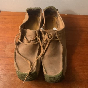 Clarks Originals wallabees mockaskor - Beiga Clarks Originals wallabees med ovandel i mocka och gummisula. Skorna har snörning och en klassisk, fyrkantig form med platt sula. Står fel storlek och modell på kartongen. Skorna har aldrig använts och har legat i sin kartong på vinden i ett bra tag. Är osäker på vad skorna är värda så är villig att förhandla ner priset 