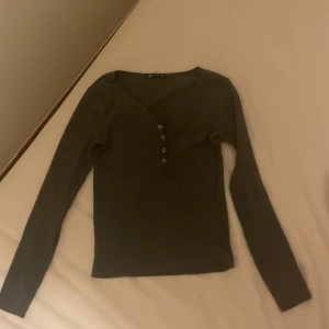 Mörkgrå ribbad topp från Zara - Mörkgrå långärmad topp från Zara i ribbat materia som ger elena girlbert vibe ifall man är intresserad av detl. Toppen har v-ringning med fyra dekorativa knappar framtill men den har dock fler knappar som man på sista bilden ser att jag har sytt bort men om man inte gillar det så kan man enkelt sprätta upp annars är den i bra skick💕💕 skriv om ni har fler frågor eller vill ha fler bilder och pris går att diskutera🩷