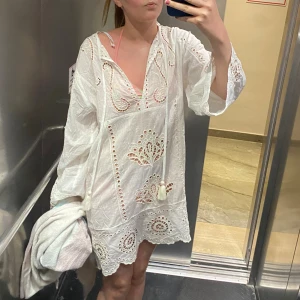 Vit strandklänning  - Superfin vit strandklänning med broderade detaljer och hålmönster. Klänningen har v-ringning med snörning och vida ärmar. Den är i storlek xs och köpt i Spanien på Primark. Använd två gånger!! 🥰🥰
