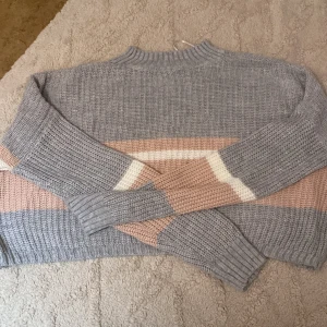 Randig stickad tröja i grått och beige - Supermysig stickad tröja med breda ränder i grått, beige och vitt. Tröjan har en högre ribbad hals och långa ärmar. Perfekt för lager på lager och chill dagar. Snygg till både jeans och kjol. Vet tyvär inte vilken storlek den är eller vart den kommer ifrån men är knappt använd och ska va lite oversized 