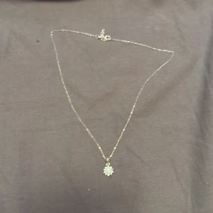 Smyckeset i silver med blomformad design - Säljer ett matchande smyckeset med halsband och ring i silverfärg. Båda har en gnistrande blomformad detalj med små stenar som ger en lyxig känsla. Perfekt för dig som gillar stilrena och eleganta accessoarer med lite extra bling.