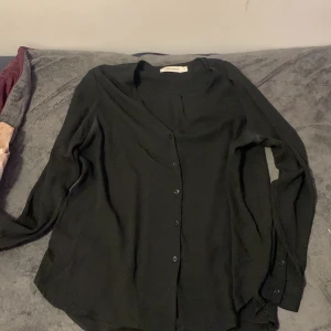 Svart skjorta från Carin Wester - Stilren svart skjorta från Carin Wester i storlek 40. Skjortan har lång ärm, klassisk krage och knappar framtill. Materialet känns mjukt och lätt, perfekt för dig som gillar minimalistisk och clean look. Passar dig som vill ha en enkel men snygg skjorta.