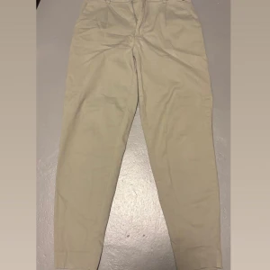 Beiga/olive chinos från Cubus - Byxorna har klassisk passform med raka ben, bälteshällor, knapp och dragkedja framtill samt två bakfickor. Perfekta för en clean och stilren look.
