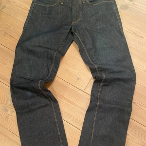 Acne Max Raw jeans mörkblå 30/32 - Säljer ett par Acne Max Raw jeans i mörkblå denim med klassisk femficksdesign och kontrastsömmar. Raka ben och normal passform. Tillverkade i 100% bomull, snyggt Acne-läderpatch bak i midjan. Perfekta för dig som gillar stilrena och tidlösa jeans.