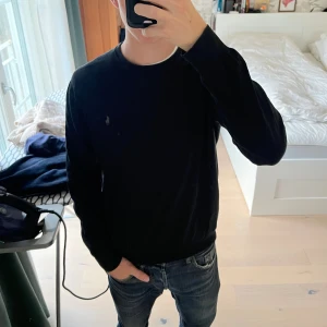Svart långärmad tröja från Polo Ralph Lauren - Svart långärmad tröja från Polo Ralph Lauren med klassisk rund hals och diskret broderad logga på bröstet. Tröjan är i mjuk bomull och har en enkel, stilren design som funkar till jeans eller chinos. Perfekt för dig som gillar clean och tidlös stil.