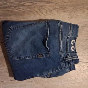 Dondup Geroge  - Säljer ett par klassiska blå jeans med snygga sömmar och detaljerad bakficka. Jeansen har bälteshällor och metallknappar framtill. Perfekta för dig som gillar en tidlös denimlook.