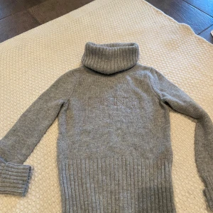 Grå polotröja från DKNY Jeans - Snygg grå polotröja från DKNY Jeans med broderad logga framtill. Tröjan är stickad i mjukt material och har bred ribbad polokrage samt muddar vid ärmslut och nederkant. 