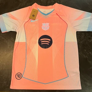 Barça Lamine Yamal 10 Nike fotbollströja - Snygg FC Barcelona fotbollströja från Nike i rosa och ljusblått med vita detaljer. Tröjan har korta ärmar, klubbmärke, Spotify-logga och Lamine Yamal 10 på ryggen. Tillverkad i lätt och ventilerande material, perfekt för match eller träning. Helt ny 💯