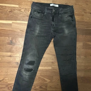 Replay Maestro Denim Selection svarta jeans med slitningar - Svarta jeans från Replay Maestro Denim Selection med coola slitningar och patchade detaljer på benen. Jeansen har klassisk femficksdesign, knapp och dragkedja fram samt svarta läderdetaljer vid fickorna. Passformen är smal och materialet är stretchigt jeans. Storlek 29/30. Pris går att diskutera vid snabb affär!👌