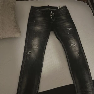 Svarta Dsquared2 Pac-Man jeans slim fit - Unika svarta jeans från Dsquared2 x Pac-Man med slim fit och coola slitningar samt färgstänk. Jeansen har klassisk femficksdesign, knappgylf och snyggt Pac-Man-märke bak. Perfekt för dig som vill sticka ut med streetstyle.