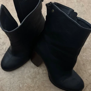 Svarta boots med klack och dragkedja - Snygga svarta boots i skinn med grov klack och rund tå. Skorna har en cool dragkedja baktill i metall och en stilren design som passar till många outfits. Perfekta för dig som vill ha en edgy men klassisk look.