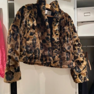 Leopardmönstrad pälsjacka croppad - Säljer en croppad pälsjacka med leopardmönster i bruna och svarta toner. Jackan har lång ärm och fluffig, mjuk känsla som ger en riktigt cool vibe. Perfekt för dig som vill sticka ut med ett djuriskt statement-plagg.