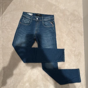 Replay Hyperflex blå jeans - Säljer ett par Replay Hyperflex jeans i klassisk blå tvätt med snygga kontrastsömmar och femficksdesign. Jeansen har normal passform och raka ben, med en skinnpatch bak i midjan. Materialet är stretchigt för extra komfort och rörelsefrihet. Dessa jeans är i mycket bra skick och är i strl 29/32.