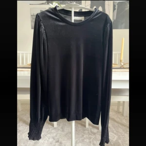 Svart sammetsblus från InWear - Supersnygg svart blus från InWear i mjuk sammet med rund hals och långa ärmar. Ärmsluten har breda, ribbade muddar som ger en cool detalj. Perfekt för dig som gillar stilrena plagg med lite extra edge.Helt ny med tagg.