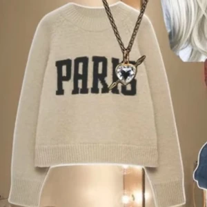 Populära paristjocktröjan - Snygg beige stickad tröja med svart text 'PARIS' framtill. Tröjan har rund hals, ribbade muddar och är långärmad. Perfekt för dig som gillar en chill och trendig stil med lite Paris-vibe. Btw så kostar den 4000 ny och fick hem igår så du får 50% av även om den e ny😚