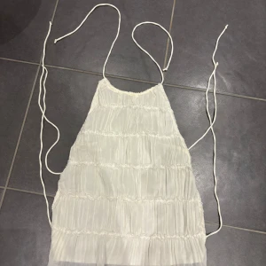 Vit knyttopp med snörning - Supersöt vit topp med tunna knytband och snörning i sidorna. Toppen har ett skirt, plisserat tyg med volangdetaljer och omlottkänsla. Perfekt för sommarens varma dagar och ger en romantisk vibe. Endast använd 1 gång 