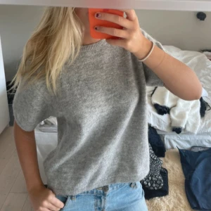 Grå stickad tröja med kort ärm - Säljer en enkel och snygg grå stickad tröja med korta ärmar och rund hals. Perfekt att matcha med jeans eller kjol för en chill och stilren look. Mjuk och skön kvalitet som passar året runt. Passar mig som är s 