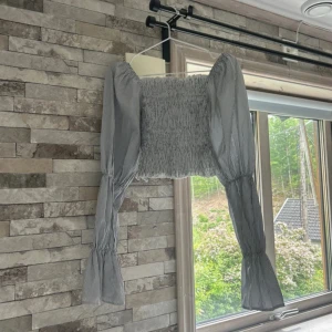 Randig croppad blus från NA-KD - Säljer en snygg croppad blus från NA-KD i storlek XXS. Blusen är vit med svarta ränder, har puffiga långärmar med resår vid ärmslut och smockad kropp. Perfekt för dig som gillar trendiga detaljer och en cool siluett.