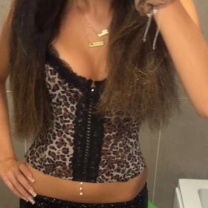 Leopardmönstrad korsett med spets - Säljer en snygg leopardmönstrad korsett med svarta spetsdetaljer och snörning framtill. Toppen har smala axelband och markerad byst, perfekt för att skapa en trendig look. Färgerna går i beige, brun och svart med coola kontraster.