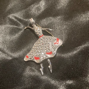 Silverfärgad ballerina brosch - äkta  - Unik brosch i form av en dansande ballerina i silverfärgad metall med glittriga detaljer och röda accenter på klänningen. Broschen har en elegant och lekfull design som verkligen sticker ut. Perfekt accessoar för dig som vill ha något annorlunda. / antik 