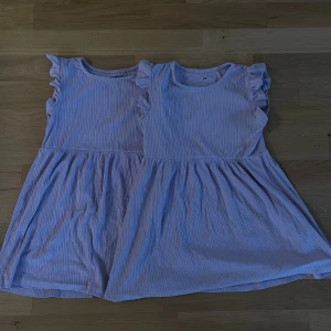 2 Ljuslila klänningar med volangärm H&M - Supersöta ljuslila klänningar från H&M med smala vertikala ränder och volangdetaljer på axlarna. Klänningarna är ärmlösa, har rund halsringning och är tillverkad i mjuk bomull. Perfekt för sommarens varma dagar och har en flowy kjol som ger en skön känsla.