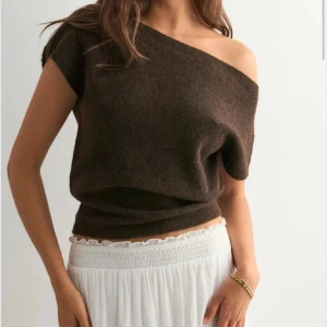Brun stickad offshoulder topp - Säljer en brun stickad topp med offshoulder-design. Toppen har en loose passform och är ärmlös, vilket ger en chill och trendig vibe. Perfekt att styla med höga kjolar eller jeans för en cool look.