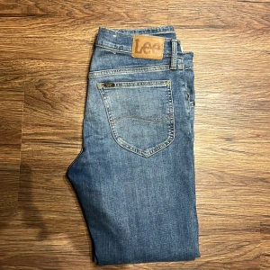 Lee Daren Zip Fly blå jeans W31 L30 - Snygga blå jeans från Lee, modell Daren Zip Fly. Klassisk femficksdesign med dragkedjegylf och Lee-lapp bak i midjan. Jeansen har en rak passform och är tillverkade i mjukt denimtyg av bomull. Perfekta för dig som gillar en tidlös och avslappnad stil.