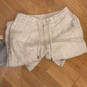 Beiga linneshorts från Bruun & Stengade - Snygga beiga linneshorts från Bruun & Stengade i slim fit-modell. De är endast använda en sommar vilket gör dem till näst intill nyskick. Bruun & Stengade tenderar även att ha bättre kvalitet jämfört med till exempel H&M. Skulle tro att de blev köpte för ca 500 men är inte helt säker. Mitt pris är iaf 149kr