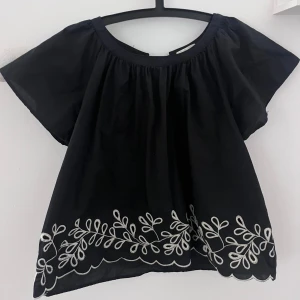 Svart blus med broderi och knyt - Säljer min jättefina blus från H&M! Nedtill finns vitt broderat mönster och vågig kant. Baksidan har en öppning med knytband. Den har en lös passform! Blusen är i storlek L men sitter bra på mig som brukar ha xs/s, eftersom den är liten i storlek💕