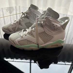 Nike Air Jordan 6 sneakers vit/grön - Nike Air Jordan 6 sneakers i vitt och ljusgrönt med högt skaft och perforerade paneler. Skorna har snörning, rund tå och detaljer i skinn och mocka. Ikonisk Jumpman-logga på hälen och en platt sula med gröna inslag. Perfekt för dig som gillar streetwear och basketstil.