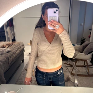 Beige omlott kofta från NA-KD - Aldrig använd, M men den sitter som S och den är stretchig. Superfin ribbad beige omlott kofta från NA-KD med v-ringning och långa ärmar. Tröjan har en snygg knytning i ryggen som ger en extra detalj. Perfekt att styla med jeans eller kjol för en chill look. 🥰🥰