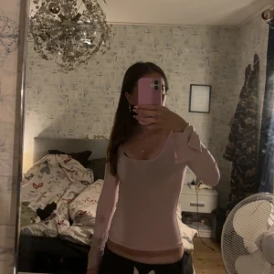 Ljusrosa långärmad topp med U-ringning - Säljer en ljusrosa långärmad topp med söt rosettdetalj på ärmen. Toppen har en tight passform och rundad halsringning, perfekt för dig som gillar en feminin och stilren look.