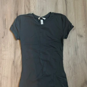 Mörk grå T-shirt hm - En enkel mörk grå t-shirt i mjuk bomull med rund hals och korta ärmar. Perfekt för en clean och stilren look. Passformen är normal och materialet känns skönt mot huden.
