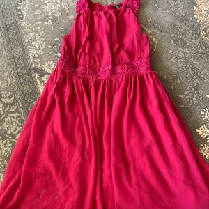 Röd långklänning med spetsdetaljer - Snygg röd långklänning från bpc med spets och paljetter i midjan och på axelbanden. Klänningen har ärmlös design och ett luftigt, svepande tyg som ger en elegant look. Perfekt för dig som vill sticka ut med färg och detaljer.