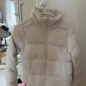 Beige teddyjacka med dragkedja - Mysig beige teddyjacka med hög krage och hel dragkedja framtill. Jackan har ett fluffigt, quiltat yttre i teddy-material och två sidofickor. Såljder för den är för lite men är helt ny! (Pris kan diskuteras) 