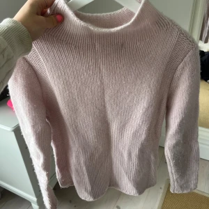 Ljusrosa stickad tröja med hög hals - Supermysig ljusrosa stickad tröja med hög hals och långärmad modell. Tröjan har en enkel, clean design utan mönster eller detaljer och är perfekt för att hålla sig varm under kyliga dagar. Passar dig som gillar en soft och chill stil.