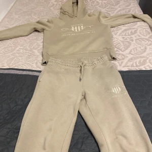 Beige hoodie från GANT med logga - Snygg beige hoodie från GANT med broderad logga och texten 'American Sportswear' på bröstet. Tröjan har huva med snörning och är tillverkad i mjuk bomullsmix. Perfekt för en chill och sportig look. Priset kan diskuteras😃