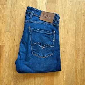Replay Anbass slim fit jeans blå - Säljer ett par Replay Anbass slim fit jeans i klassisk blå tvätt. Jeansen har fem fickor, snygga kontrastsömmar och läderpatch med Replay-logga bak. Modellen är smal och sitter riktigt schysst på benen. Perfekta för dig som gillar stilrena och bekväma jeans.