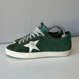 Gröna Golden Goose sneakers med stjärna - Snygga gröna sneakers från Golden Goose med vit stjärndetalj på sidan och vit sula. Skorna är tillverkade i mocka. Klassisk låg modell med rund tå och GGDB-logga. Stlr 41 men passar 42. Priset är inte hugget i sten så skicka prisförslag.