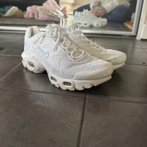 Vita Nike TNs - Säljer ett par fräscha vita Nike Tns sneakers med ikonisk Tn-detalj på hälen. Skorna har en chunky sula med synliga luftbubblor, snörning och mesh- och syntetmaterial för en sportig vibe. Perfekta för dig som gillar streetstyle och vill sticka ut.