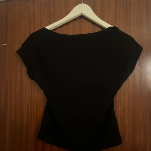 Svart topp med öppen rygg från SHEIN - Svart topp från SHEIN med djup öppen rygg och korta ärmar. Toppens material är mjukt och stretchigt, vilket gör den bekväm och smickrande. Perfekt för att skapa en stilren look med en twist. Passar dig som gillar minimalistisk stil med en detalj som sticker ut.