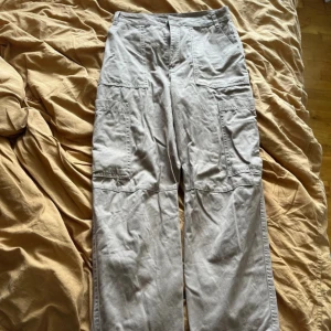 Ljusbruna cargobyxor från Monki - Säljer ett par ljusbruna cargobyxor från Monki med flera stora fickor på sidorna och baktill. Byxorna har en rak och loose passform, hög midja och är tillverkade i bomull. Perfekta för en avslappnad och trendig look.